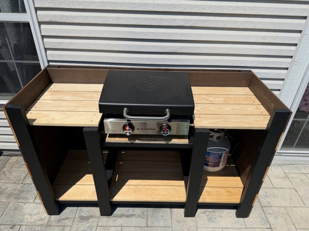 A black and wood outdoor cooking station with a Blackstone griddle built into the center countertop.
