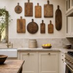 Wooden cutting boards arranged decoratively on a kitchen wall above cream cabinets and a stone countertop.