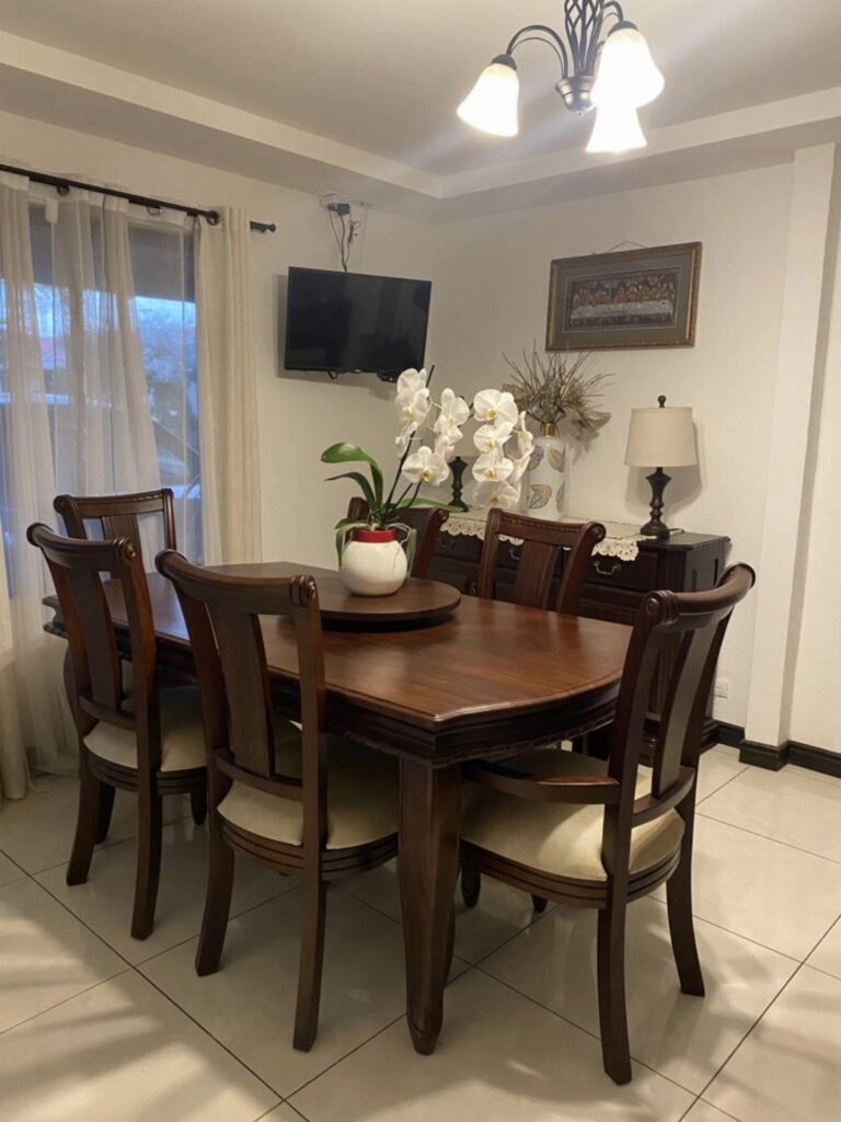 A dark wood dining table with four matching chairs and a white orchid centerpiece.