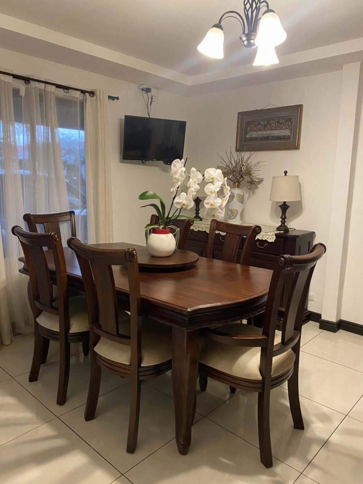 A dark wood dining table with four matching chairs and a white orchid centerpiece.