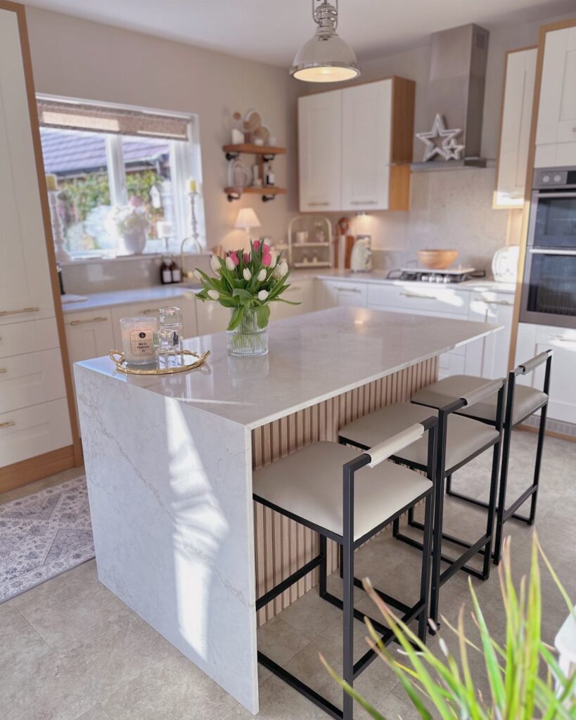 A modern kitchen island with a white waterfall countertop and wooden slat side panel with bar stools.