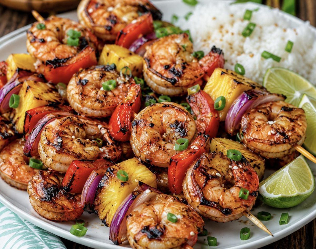 Grilled shrimp skewers with pineapple and peppers served alongside white rice and lime wedges.
