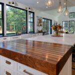 A polished dark wood butcher block surface on a white kitchen island with marble countertops.