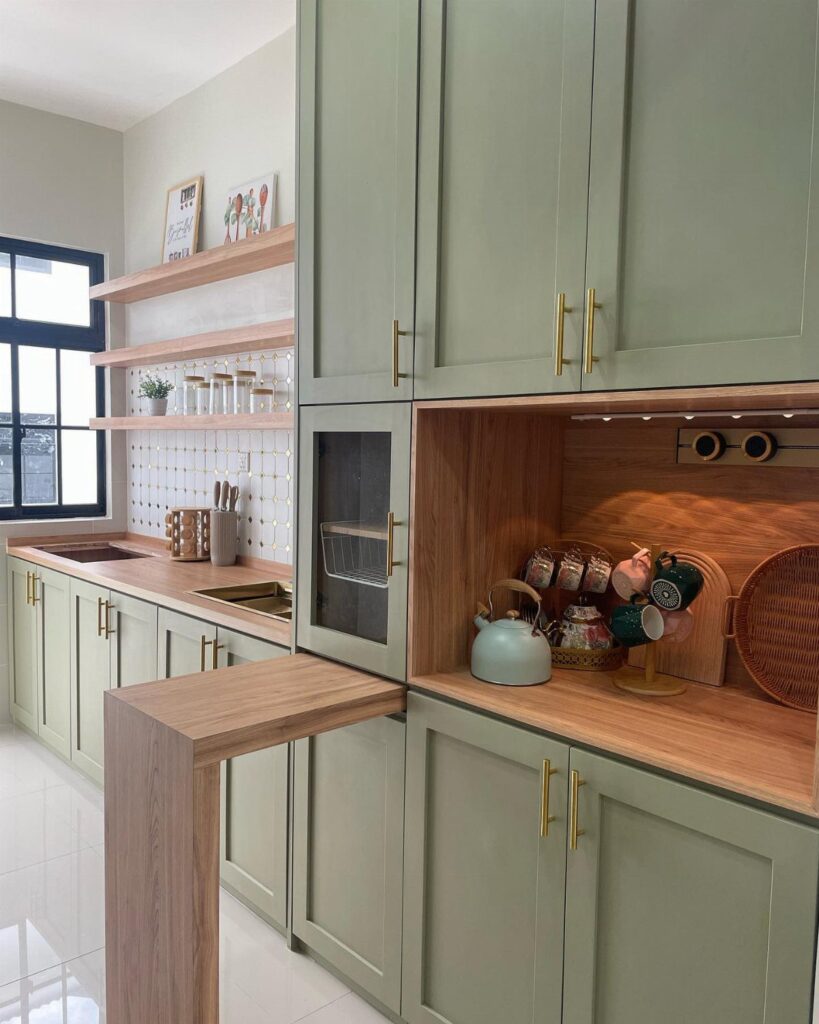 Olive green kitchen cabinets with gold hardware and light wood countertops against white tiles.