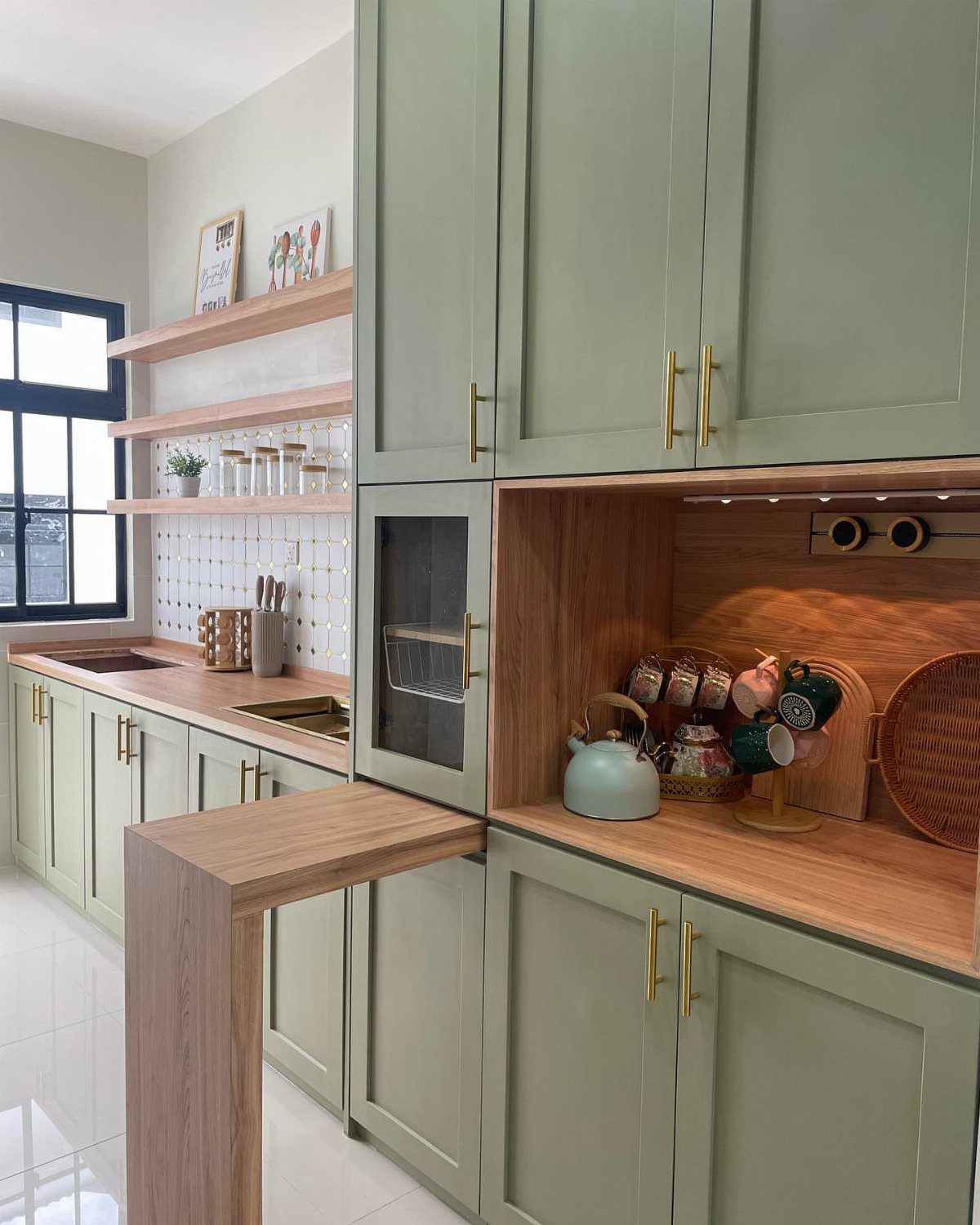 Olive green kitchen cabinets with gold hardware and light wood countertops against white tiles.