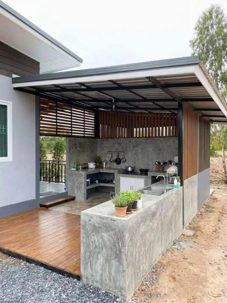 Modern outdoor kitchen with concrete counters, a sink, and wooden slat walls under a dark roof.