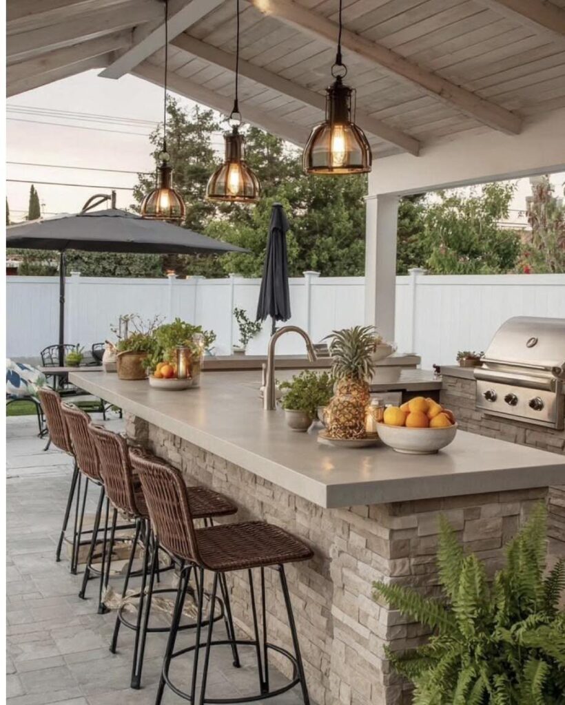 A smooth grey concrete countertop with bar stools and pendant lights in an outdoor kitchen setting.