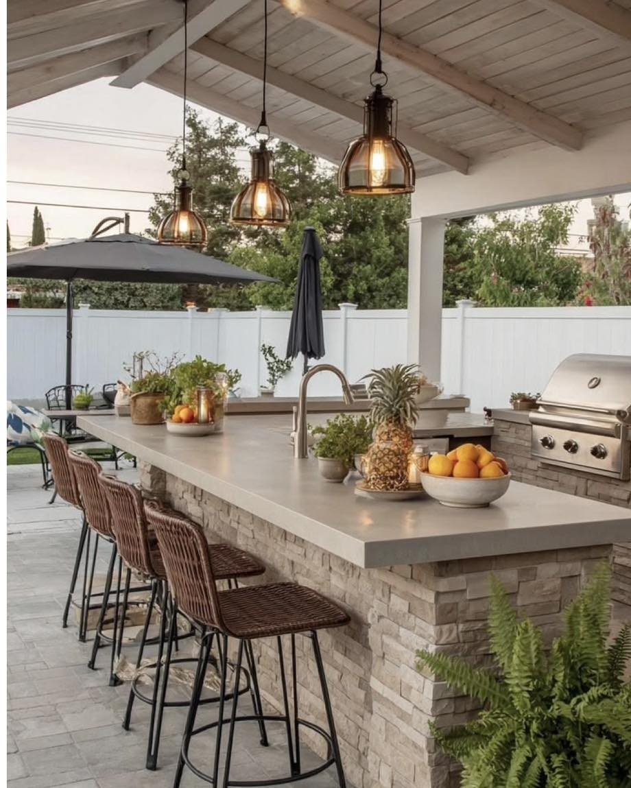 A smooth grey concrete countertop with bar stools and pendant lights in an outdoor kitchen setting.